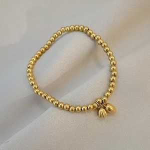 Golden beaded stretch bracelet featuring heart and tulip pendants on grey fabric