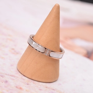Rose gold ring with white shell inlay and three small diamonds on a wooden stand