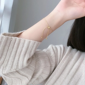 Minimalist adjustable gold snake chain bracelet on woman's wrist with knit sweater