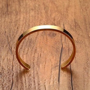 Detailed view of a minimalist gold-plated titanium steel open cuff bangle on wood