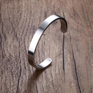 Close-up of a mirror-polished titanium steel open bangle on a dark wood background