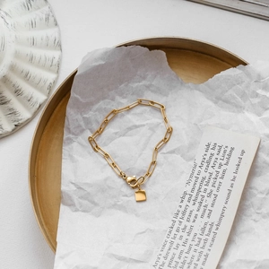 Bracelet chaîne trombone doré élégant avec pendentif carré sur fond minimaliste