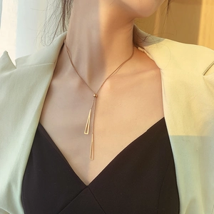 Detail of adjustable gold triangle tassel necklace shown on a model neck in soft light