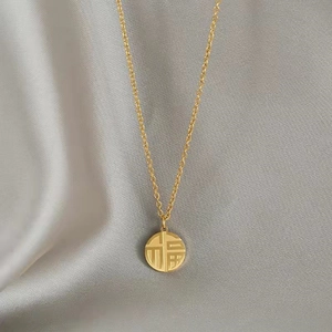 Détail macro du pendentif doré Fu sur tissu en soie avec une fine chaîne élégante