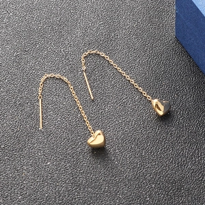Polished 18k gold heart drop earrings with long threader chains on dark background