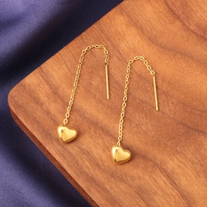 Polished 18k gold heart drop earrings on dark silk and wooden background