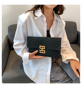 Detail einer schwarzen gesteppten Umschlag-Clutch mit goldenem Verschluss im Lifestyle-Look