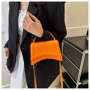 Détail d'un sac à main orange vibrant porté sur un tailleur noir élégant et moderne