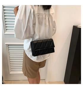 Close-up of black quilted shoulder bag with silver chain strap worn by a model
