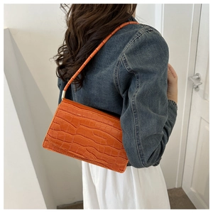 Detail of bright orange crocodile texture on a patent leather baguette shoulder bag