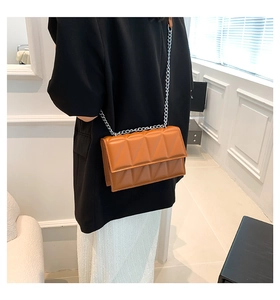 Close-up of brown quilted chain bag with geometric pattern on woman's shoulder