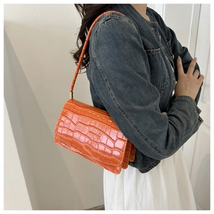 Detail of a bright orange crocodile pattern baguette bag worn on a shoulder