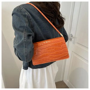 Close-up of bright orange crocodile pattern leather shoulder bag on blue denim jacket