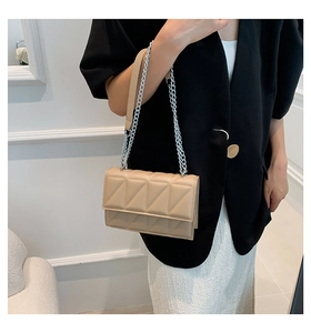 Detail of beige quilted shoulder bag with chain strap worn with a black blazer