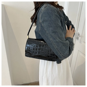 Lifestyle shot of black crocodile embossed patent leather shoulder bag on a model