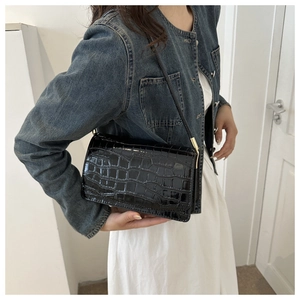Close-up of black croc-effect shoulder bag with gold hardware worn by a model