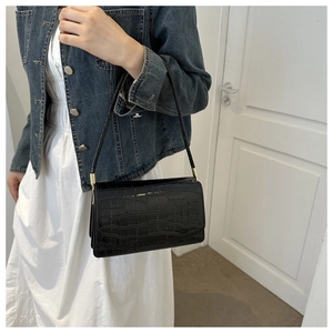 Close-up of black crocodile embossed shoulder bag with gold metal cylindrical hardware