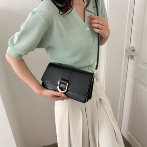 Minimalist black flap crossbody bag with gold U-shaped buckle on a female model