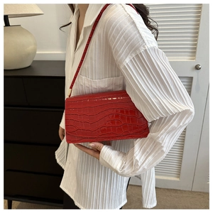 Macro detail of red faux crocodile leather texture and glossy finish on shoulder bag