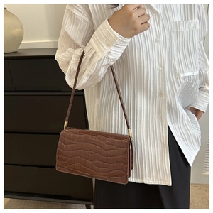 Close-up of a dark brown crocodile pattern handbag worn by a model with gold hardware