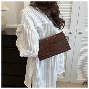 Detail of vintage brown crocodile pattern baguette bag with glossy texture and gold metal hardware