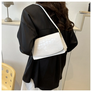 Detail of white crocodile pattern shoulder bag with gold hardware on black silk shirt