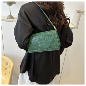 Detail of green crocodile embossed shoulder bag on model with glossy patent finish