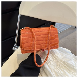 Macro detail of glossy orange crocodile pattern texture on a leather shoulder bag