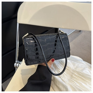 Detail of black faux crocodile leather shoulder bag with glossy finish and gold hardware