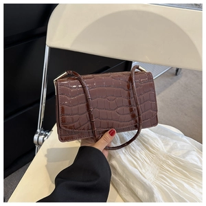 Detail of dark brown crocodile textured glossy handbag with golden metal hardware