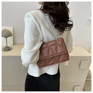 Detail of a brown quilted leather crossbody bag with geometric stitching and silver chain