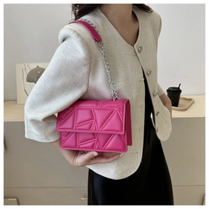 Detail of rose red quilted crossbody bag with silver chain strap on model shoulder