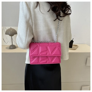Detail of rose red quilted chain bag worn by model in minimalist indoor setting