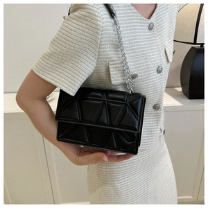Detail view of a black geometric quilted crossbody bag with silver chain on model
