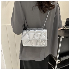 Close-up of silver quilted crossbody bag with metallic texture and chain strap on model