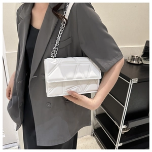 Close-up of a white rectangular chain bag with geometric quilted pattern on a grey suit