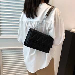 Chic black quilted crossbody bag with silver chain strap shown on a white shirt model