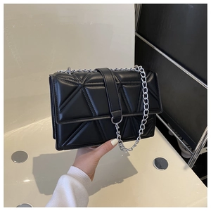 Detailed view of black quilted crossbody bag with geometric triangle stitching and metal chain