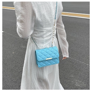 Petit sac bandoulière matelassé bleu clair avec chaîne en perles porté sur robe blanche
