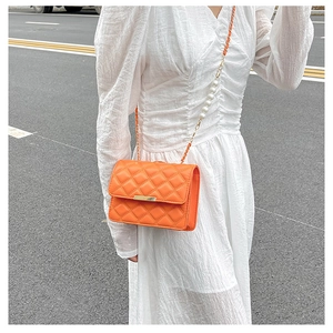 Détail d'un petit sac matelassé orange avec boucle dorée et bandoulière en perles chics
