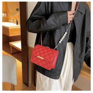 Détail d'un sac bandoulière rouge matelassé avec boucle dorée et chaîne en perles chic