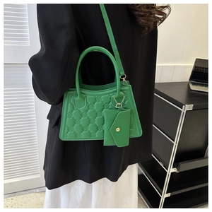 Detail of green quilted handbag with embossed logo and matching mini pouch accessory