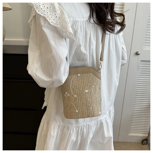 Detail of woven straw bucket bag with floral embroidery and leather crossbody strap