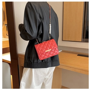 Détail du sac bandoulière rouge matelassé avec de grandes perles blanches sur chaîne dorée