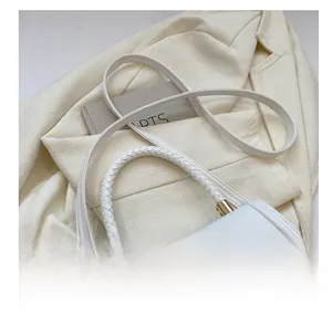Close-up of white leather handbag with woven handle and gold metal lock on a suit