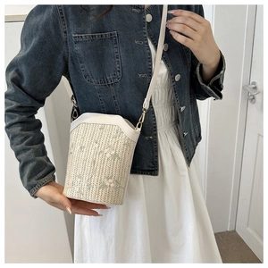 Detail of straw bucket bag with floral embroidery and white leather strap on model