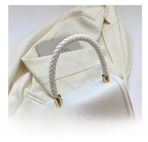 Close-up of white leather handbag featuring woven handle and golden twist lock closure