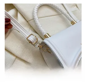 Close-up of golden metal hooks and woven round handle on a white fashion handbag