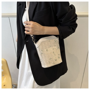 Close-up of woven bucket bag with floral embroidery and white faux leather strap