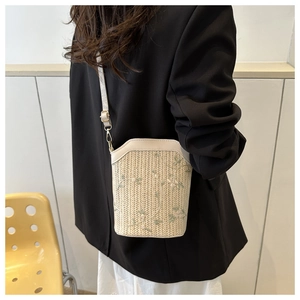 Detail of hand-woven straw bucket bag featuring delicate floral embroidery and leather strap